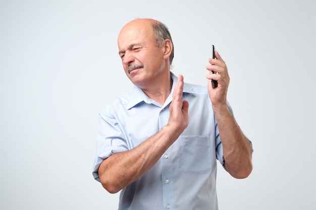 Bel homme mature refusant de parler au téléphone sur fond isolé en détournant son visage