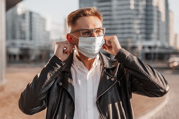 Bel homme mettant un masque de protection médicale sur son visage avec des lunettes dans une grande rue de la ville sur fond urbain