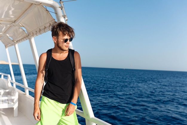 bel homme à la mode en lunettes de soleil et short sur un yacht lors d'un voyage à la mer