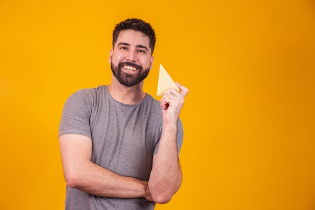 Bel homme avec morceau de fromage sur fond jaune. Garçon avec une tranche de fromage à la main