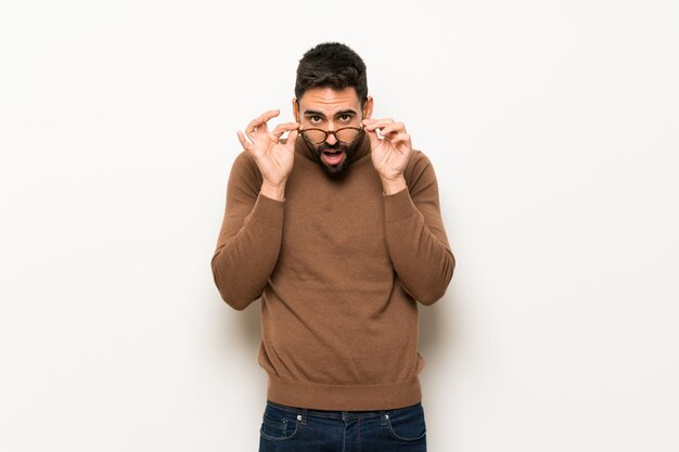 Bel homme sur un mur blanc avec des lunettes et surpris