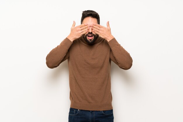 Bel homme sur un mur blanc qui couvre les yeux à la main. Surpris de voir ce qui nous attend