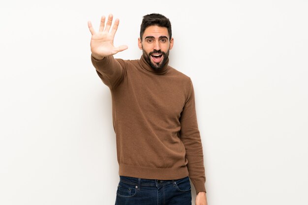 Bel homme sur un mur blanc, saluant avec la main avec une expression heureuse