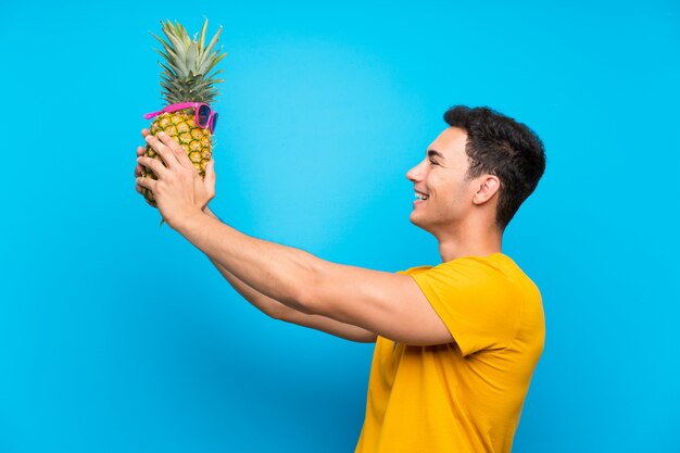 Bel homme sur mur bleu tenant un ananas avec lunettes