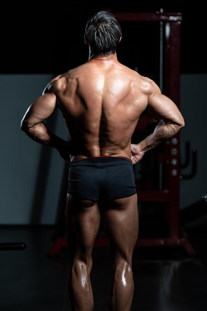 Bel homme mûr debout fort dans la salle de gym et muscles de la flexion - modèle de forme physique athlétique musclé posant après les exercices