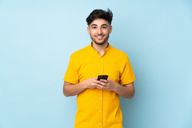 Bel homme sur un mur isolé en envoyant un message avec le mobile