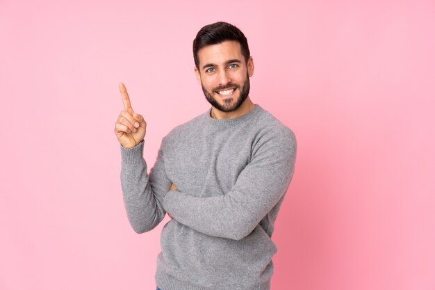 Bel homme sur mur isolé heureux et pointant vers le haut