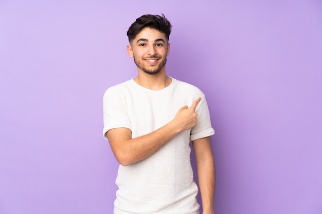 Bel homme sur un mur isolé pointant vers le côté pour présenter un produit