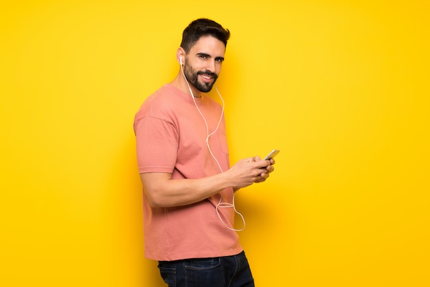 Bel homme sur un mur jaune, envoyant un message avec le téléphone portable