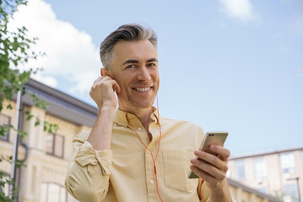 Bel homme mûr tenant un téléphone mobile, écouter de la musique, regardant la caméra, souriant