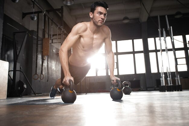 Bel homme musclé faisant des exercices de pompes avec haltères dans un entraînement crossfit.