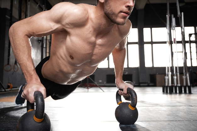 Bel homme musclé faisant des exercices de pompes avec haltères dans un entraînement crossfit.