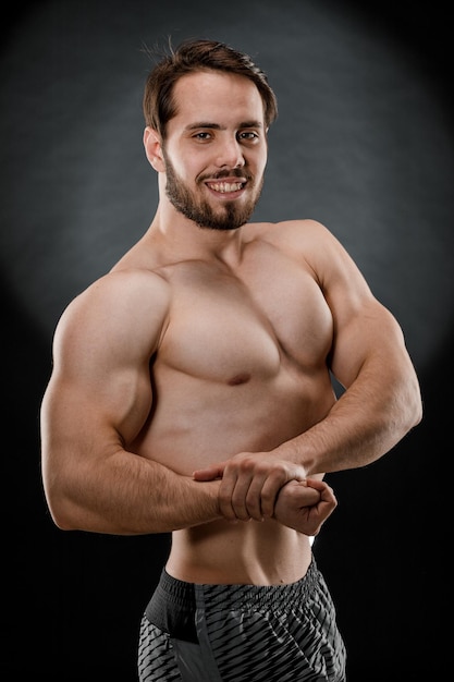 Un bel homme musclé sans t-shirt pose pour un photographe dans un studio photo sombre