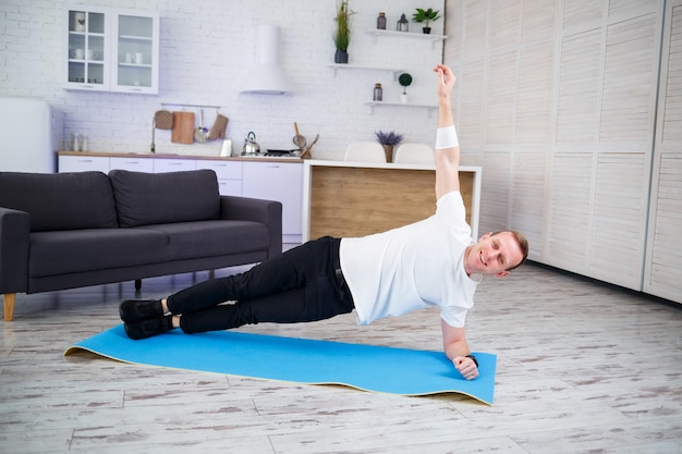 Un bel homme musclé en t-shirt fait des exercices fonctionnels sur le sol à la maison. Remise en forme à la maison. Mode de vie sain.