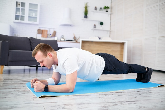 Un bel homme musclé en t-shirt fait des exercices fonctionnels sur le sol à la maison. Remise en forme à la maison. Mode de vie sain.