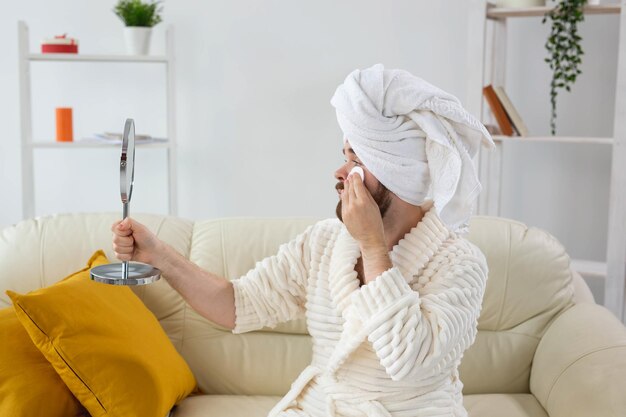 Bel homme nettoyant la peau du visage avec des tampons de coton et regardant le corps et la peau du spa miroir