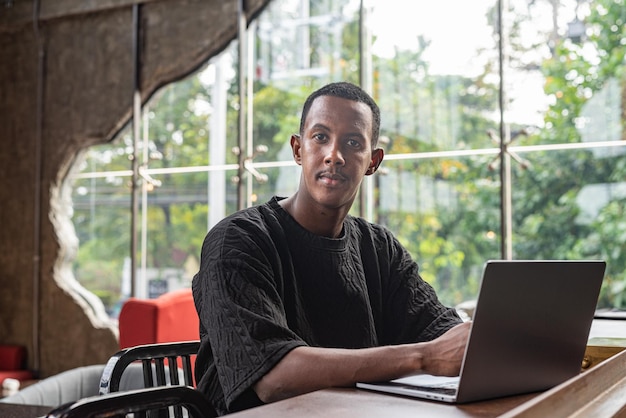 Bel homme noir assis et utilisant un ordinateur portable à l'intérieur