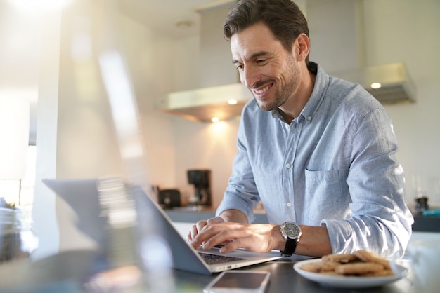 Bel homme avec ordinateur dans cuisine moderne