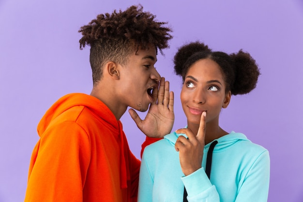 Bel homme parlant à l'oreille de la jeune femme, isolé sur mur violet