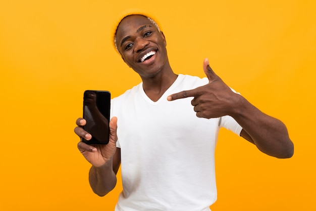 Bel Homme à La Peau Foncée Souriant Dans Un T-shirt Blanc Est Titulaire D'un Smartphone Sur Orange