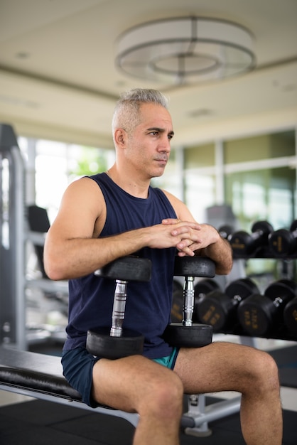 Bel homme persan mûr s'exerçant avec des haltères et s'asseyant au gymnase