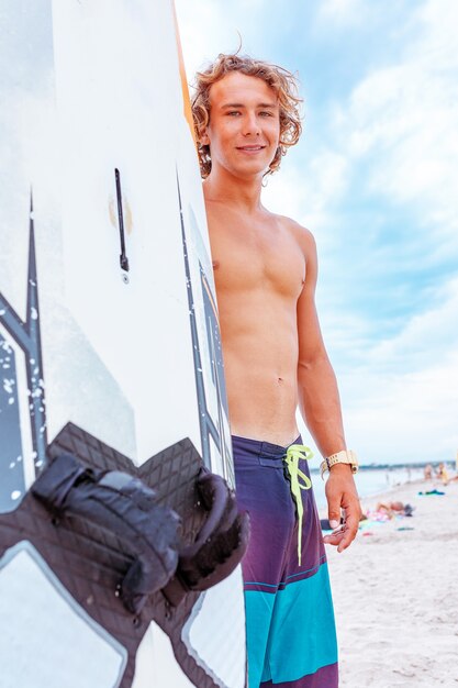 Bel homme à pied avec planche de surf vierge blanche attendre la vague de surf spot au bord de l'océan mer