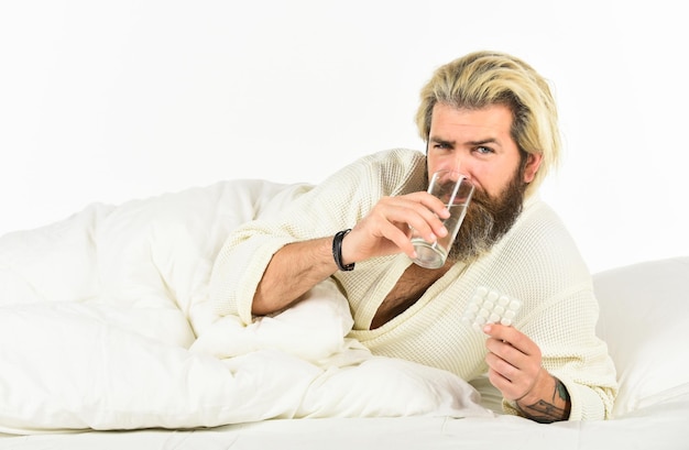 Bel homme avec pilule et verre d'eau Prendre des analgésiques Concept de traitement Soins de santé Prendre des médicaments Homme barbu en congé de maladie Soins de santé de l'homme prenant des médicaments à la maison