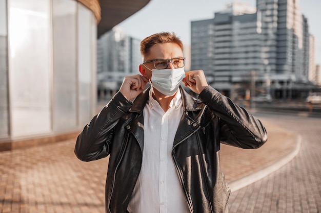 Bel homme portant un masque de protection médicale sur son visage avec des lunettes dans une grande rue de la ville sur un fond urbain