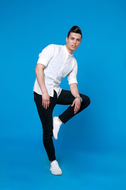 Bel homme porte une veste en cuir noir. photo pleine longueur d'un jeune homme décontracté debout avec sa veste sur son épaule et sa main dans sa poche tout en regardant dans la caméra. sur fond bleu