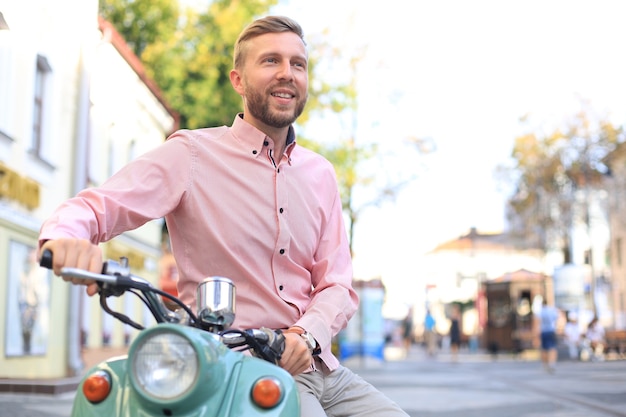 Bel homme posant sur un scooter dans un contexte de vacances. Mode et style de rue.
