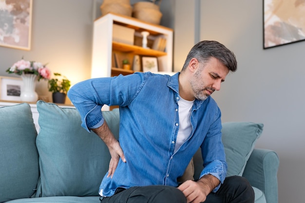 Photo un bel homme qui touche son dos souffre de maux de dos, de sciatique, d'un style de vie sédentaire, de problèmes de santé de la colonne vertébrale, d'une assurance maladie.