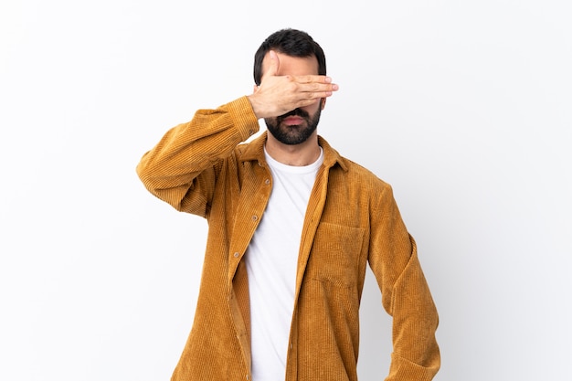 Bel homme de race blanche avec barbe portant une veste en velours côtelé sur un mur blanc isolé couvrant les yeux par les mains. Je ne veux pas voir quelque chose