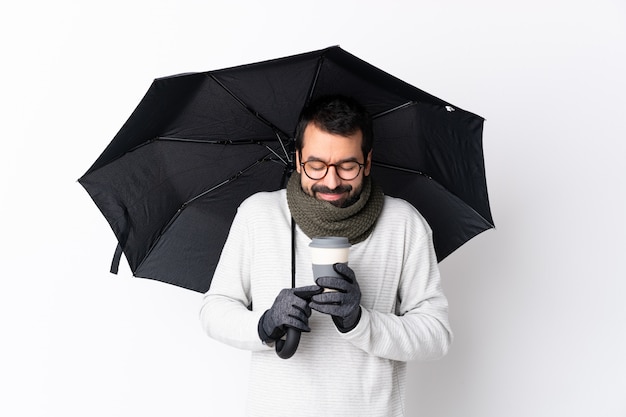 Bel homme de race blanche avec barbe tenant un parapluie et un café à emporter