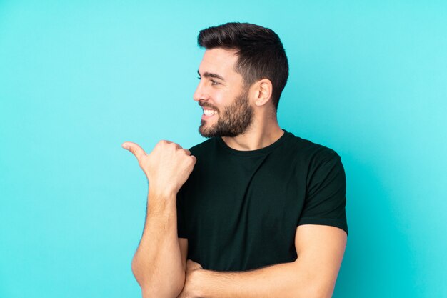 Bel homme de race blanche sur mur bleu pointant vers le côté