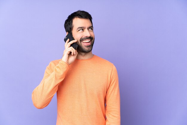 Bel homme de race blanche sur mur violet isolé, garder une conversation avec le téléphone mobile