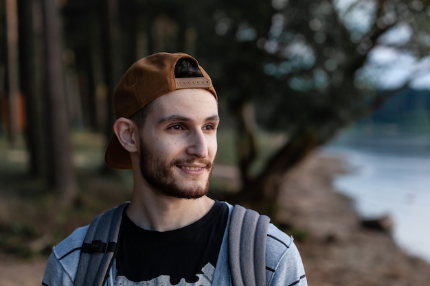 Bel homme réfléchi debout près du lac et regardant à distance avec un regard pensif