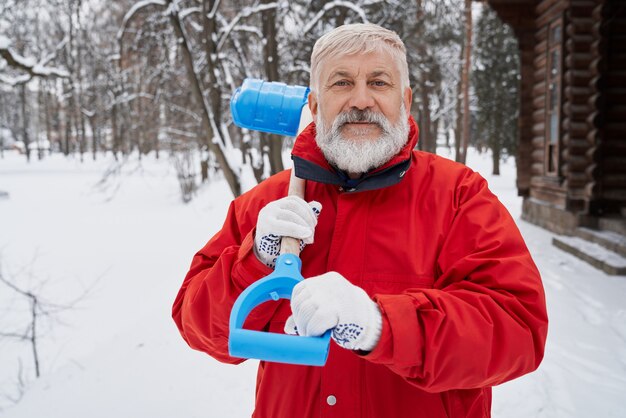 Bel homme regardant la caméra tout en enlevant la neige en hiver