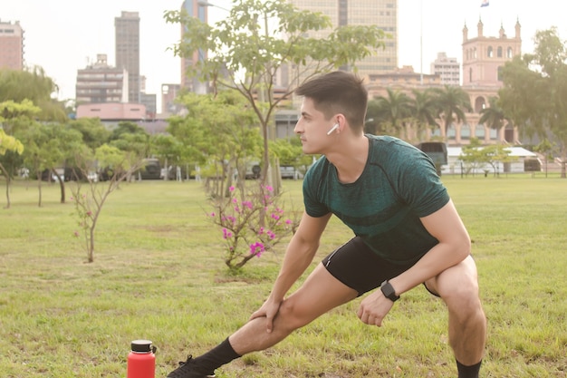 Bel homme de remise en forme qui s'étend dans le parc avec la ville en arrière-plan.