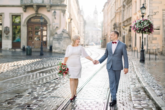 Bel homme romantique et belle femme, portant des vêtements élégants, profitant d'une promenade en ville. Portrait d'un couple amoureux d'âge moyen heureux, se tenant la main, ayant un rendez-vous dans la ville antique