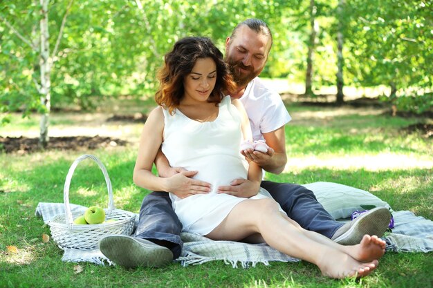 Bel homme et sa charmante femme enceinte avec des chaussons de bébé dans le parc