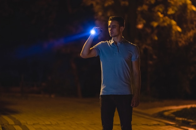 Le bel homme se tient avec une lampe de poche dans la rue sombre. la nuit
