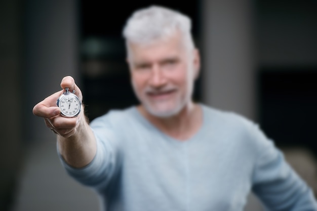 Bel homme senior aux cheveux gris avec un poids chronomètre à la main. Concept de sport et de soins de santé