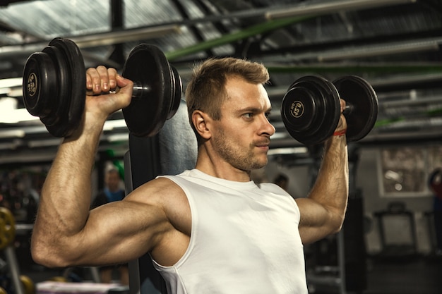 Bel homme sérieux de remise en forme, faire des exercices d'haltérophilie avec des haltères au gymnase