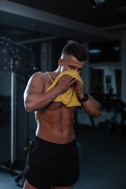 Bel homme sexy au corps musclé s'essuie le visage avec un t-shirt après une séance d'entraînement intense dans la salle de gym