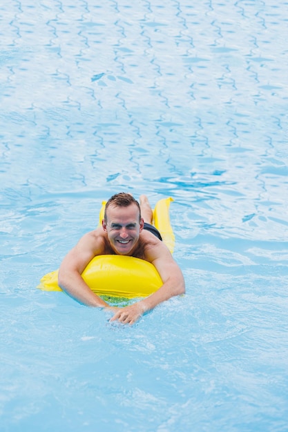 Bel homme en short de bain avec un matelas jaune gonflable dans la piscine Vacances d'été à l'hôtel