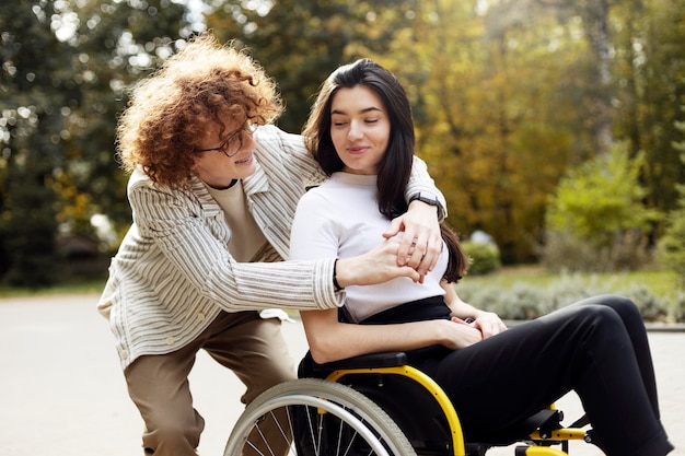 Photo bel homme souriant dans des verres aux cheveux bouclés embrasse une fille dans la rue une fille handicapée est assise dans un fauteuil roulant