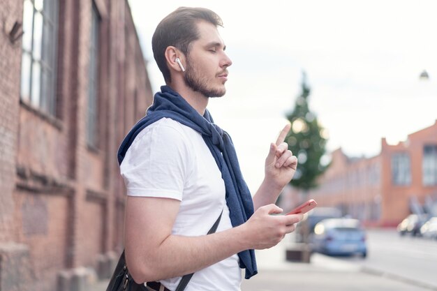 Bel homme souriant, écouter de la musique en marchant dans la ville