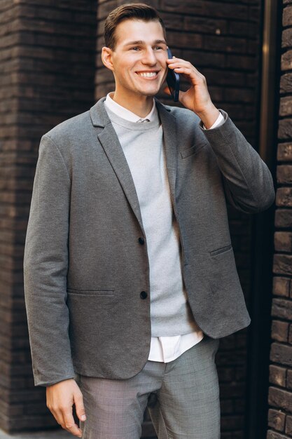 Bel homme souriant moderne marchant dans la rue et parlant au téléphone