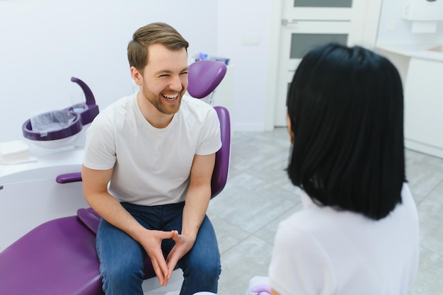 Bel homme souriant pendant l'examen des dents Heureux homme patient assis dans une chaise de dentiste et ayant vérifier les dents