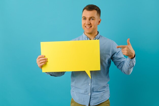 Bel homme souriant tenant un signe de bulle de dialogue vierge isolé sur fond de bannière de studio bleu clair avec espace de copie